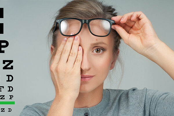 Woman with hand over eye next to an eye chart.