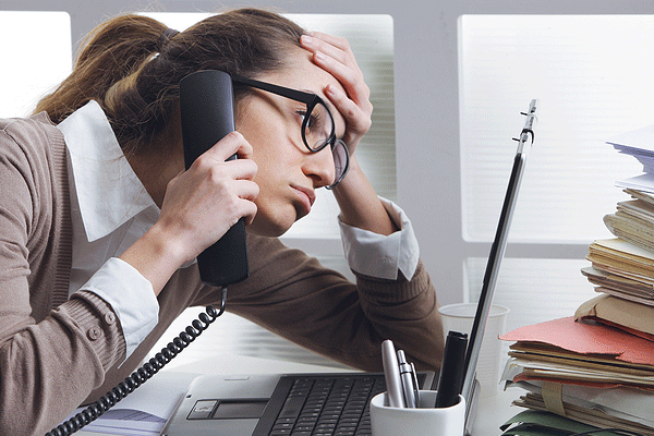 Woman sitting at a desk on the phone staring at computer and looking stressed out