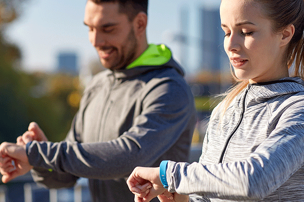 Man and woman walking outside looking at their smart watch